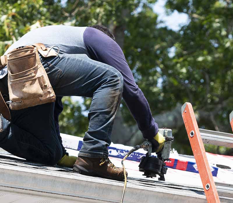 Close up of worker installing new shingles on a roof with a nail gun